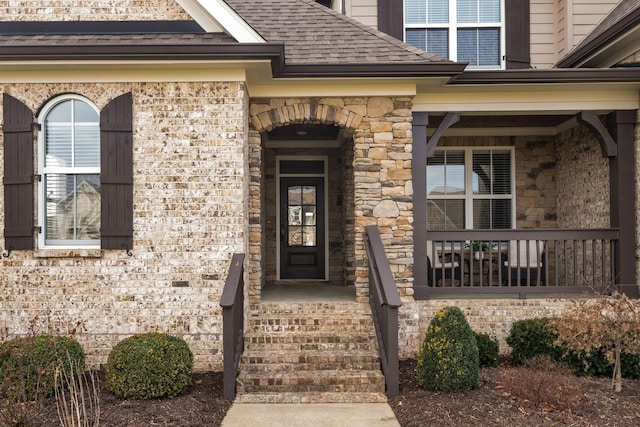 view of exterior entry featuring a porch, stone siding, and roof with shingles