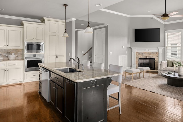 kitchen with a fireplace, crown molding, appliances with stainless steel finishes, a sink, and a kitchen breakfast bar