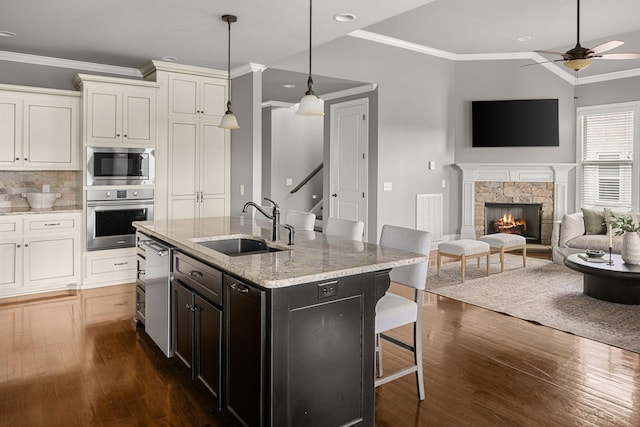 kitchen with a fireplace, a sink, appliances with stainless steel finishes, a kitchen bar, and crown molding