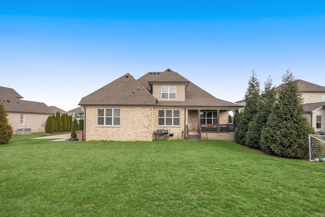 rear view of property featuring a shingled roof, brick siding, and a lawn