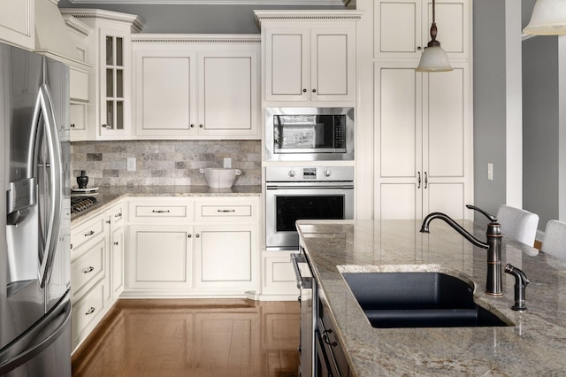 kitchen with stainless steel appliances, light stone counters, a sink, and decorative backsplash