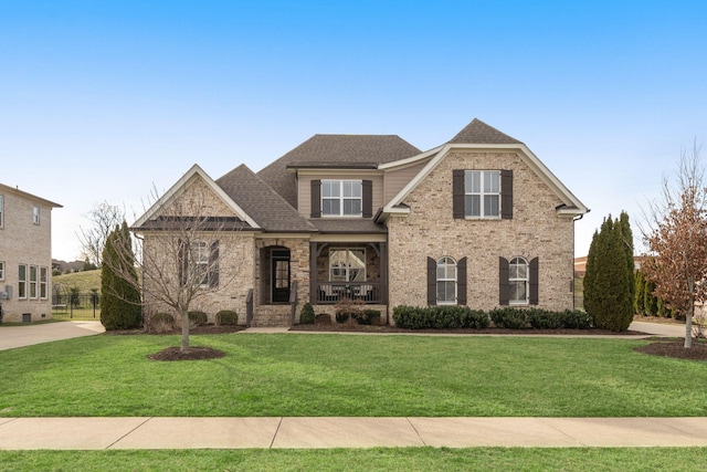 view of front of home with a front yard, brick siding, and roof with shingles