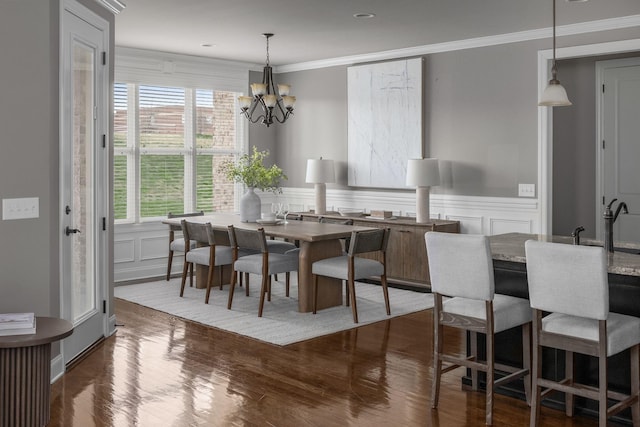 dining space featuring a chandelier, a decorative wall, dark wood finished floors, and crown molding