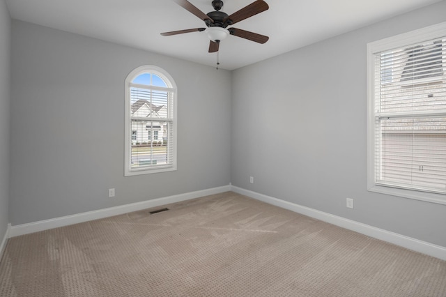 empty room with a ceiling fan, light carpet, visible vents, and baseboards