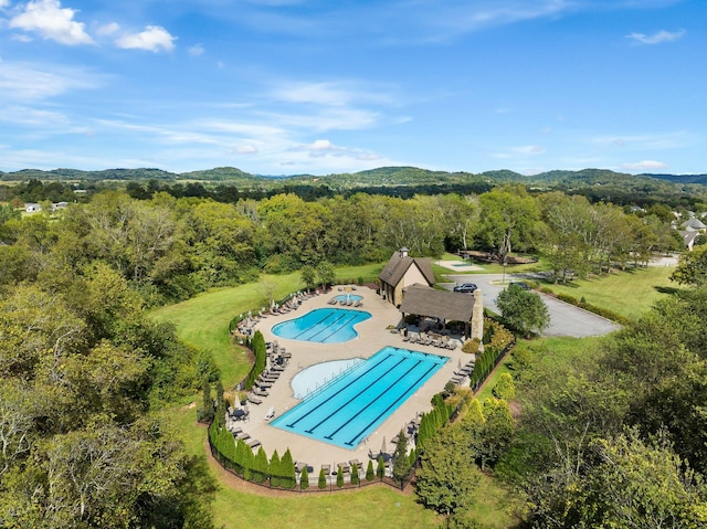 pool featuring a patio area, fence, a mountain view, and a view of trees