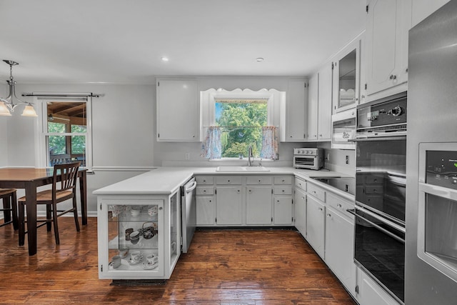 kitchen featuring dark wood-style floors, stainless steel appliances, light countertops, a sink, and a peninsula