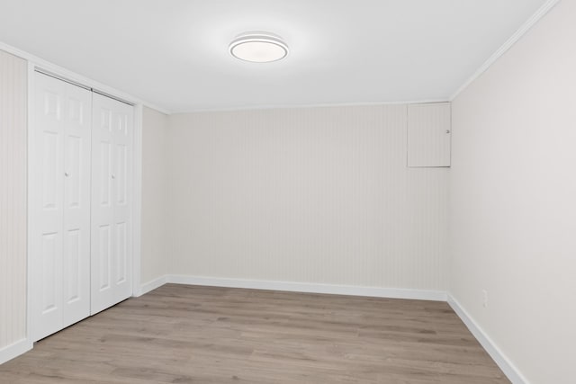 unfurnished bedroom featuring light wood-style flooring, crown molding, baseboards, and a closet