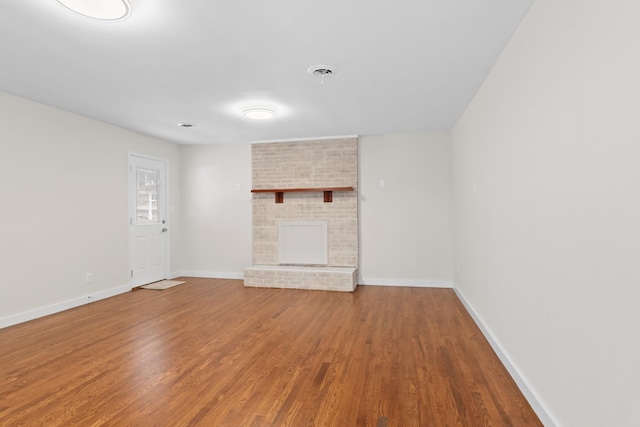 unfurnished living room with visible vents, a fireplace, baseboards, and wood finished floors