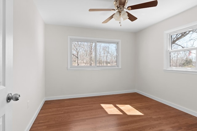 spare room with a ceiling fan, a wealth of natural light, baseboards, and wood finished floors