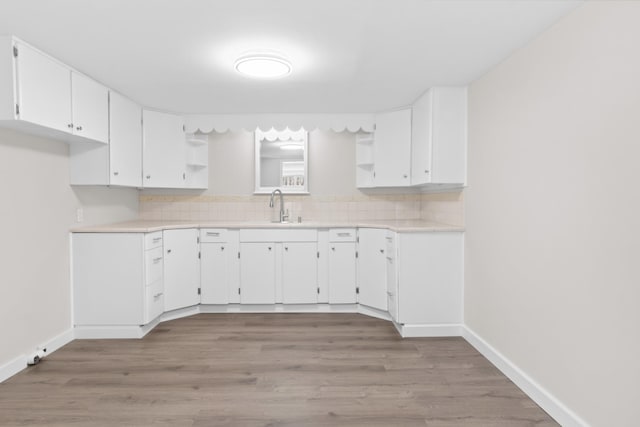 kitchen with a sink, white cabinetry, light countertops, backsplash, and open shelves