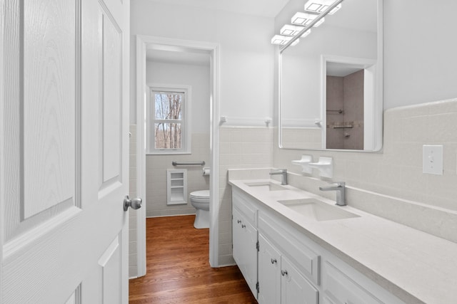 full bathroom with toilet, wood finished floors, vanity, tile walls, and wainscoting