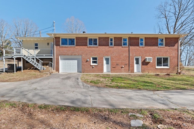 view of front of house with aphalt driveway, a garage, stairway, a wall mounted AC, and a front lawn