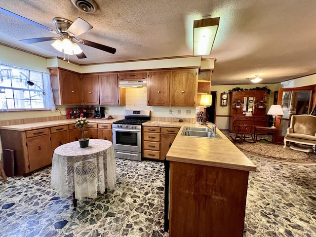 kitchen with under cabinet range hood, a peninsula, a sink, visible vents, and stainless steel gas stove