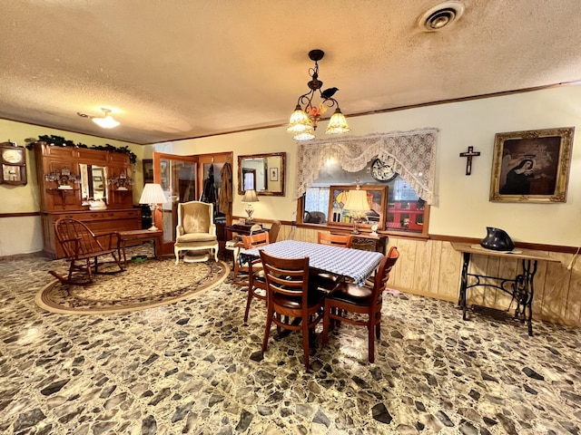 dining space with a textured ceiling, wooden walls, a wainscoted wall, visible vents, and crown molding