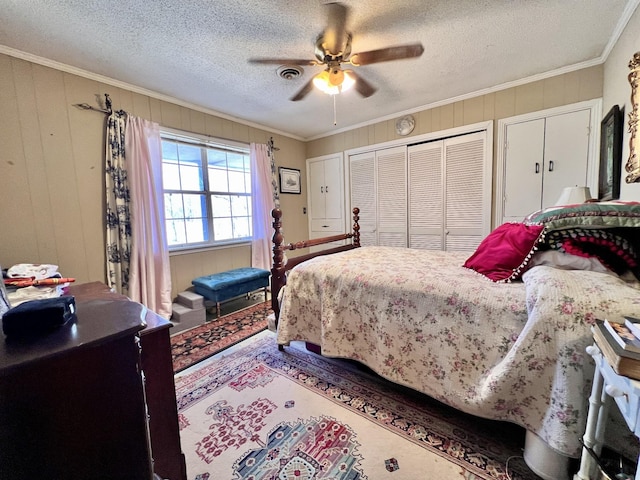 bedroom featuring visible vents, ceiling fan, a textured ceiling, crown molding, and multiple closets