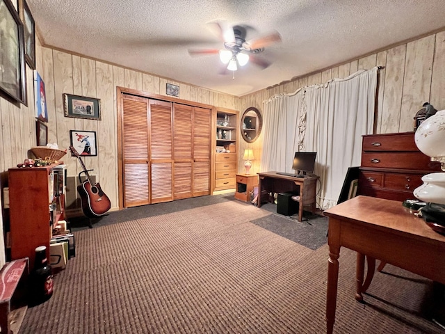 carpeted home office with a textured ceiling, ceiling fan, and wooden walls