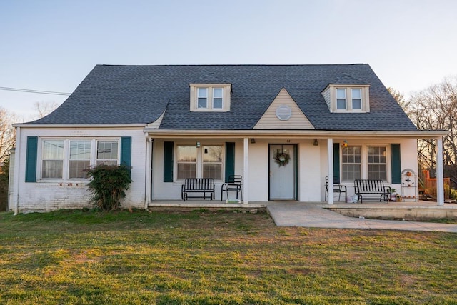 view of front facade with covered porch, roof with shingles, brick siding, and a front lawn