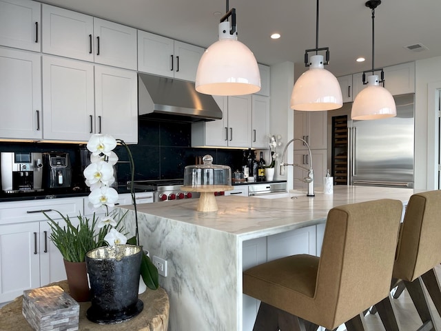 kitchen featuring under cabinet range hood, a sink, visible vents, stainless steel built in fridge, and tasteful backsplash