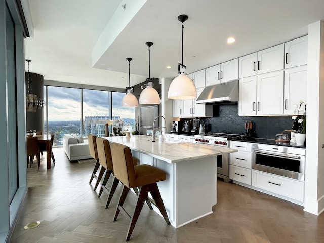 kitchen with tasteful backsplash, a breakfast bar area, appliances with stainless steel finishes, under cabinet range hood, and a sink