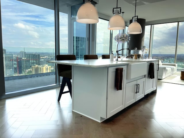 kitchen featuring a kitchen island with sink, a sink, white cabinets, hanging light fixtures, and light countertops