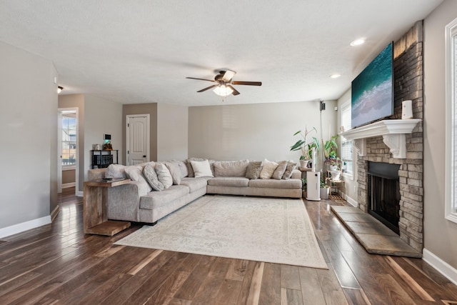 living area featuring a large fireplace, ceiling fan, dark wood-style flooring, and baseboards