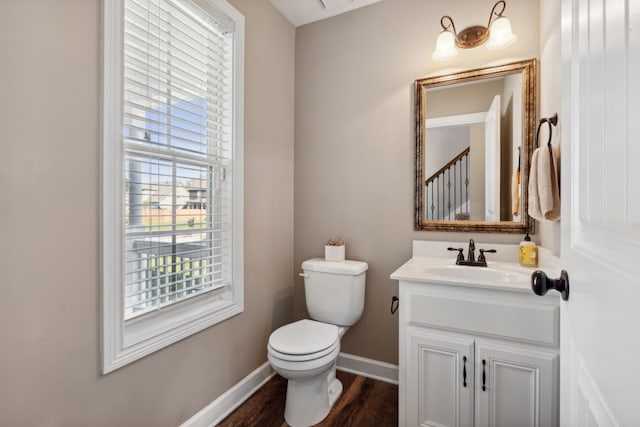 half bathroom with toilet, vanity, baseboards, and wood finished floors