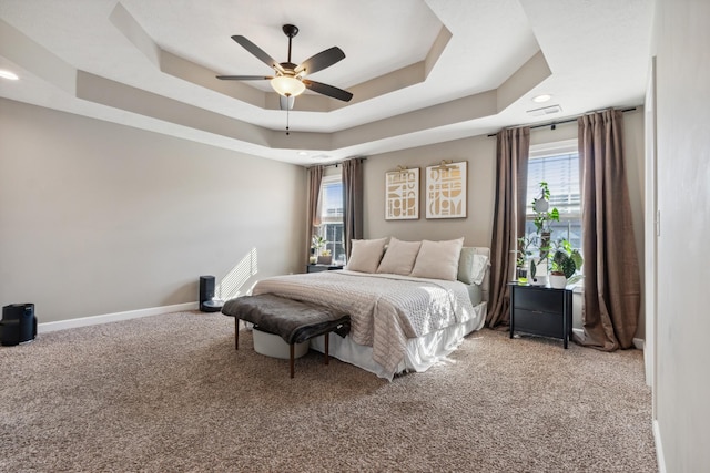 bedroom with carpet floors, a tray ceiling, multiple windows, and baseboards