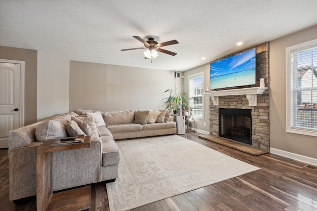 living room with a stone fireplace, plenty of natural light, wood finished floors, and baseboards