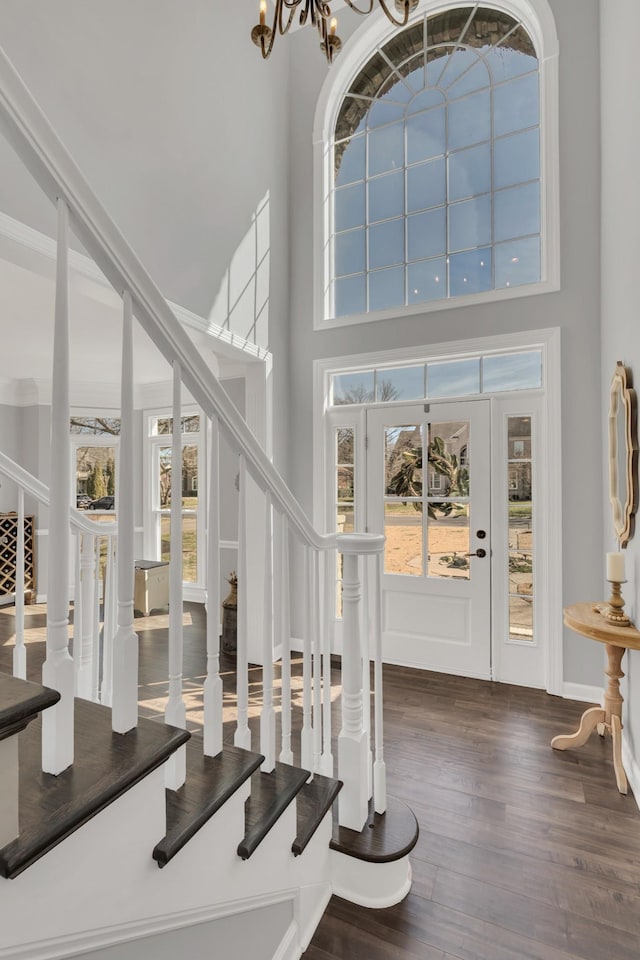 foyer entrance with a notable chandelier, wood finished floors, a towering ceiling, baseboards, and stairs