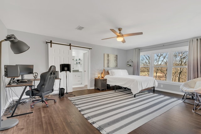 bedroom with a barn door, wood finished floors, visible vents, and baseboards