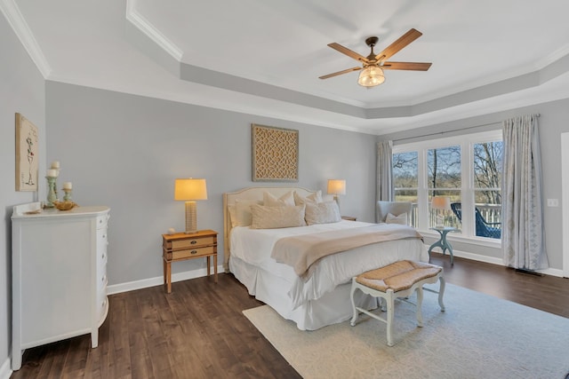 bedroom featuring dark wood-type flooring, a tray ceiling, ornamental molding, and baseboards