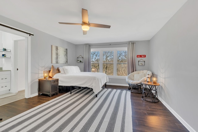 bedroom featuring ceiling fan, a barn door, wood finished floors, and baseboards