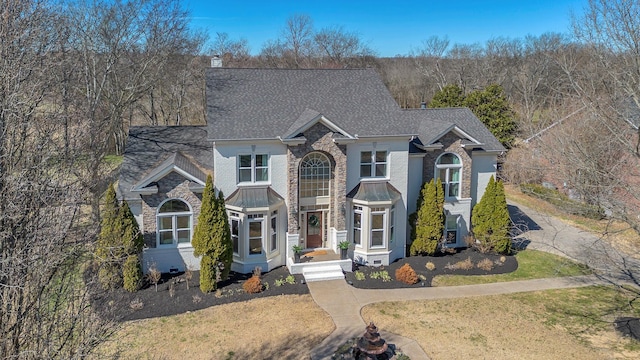 traditional home with stone siding, a chimney, roof with shingles, a standing seam roof, and a front lawn