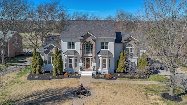 traditional home with a front yard, stone siding, and roof with shingles