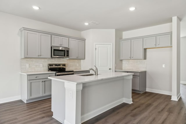 kitchen featuring dark wood-style floors, appliances with stainless steel finishes, a kitchen island with sink, gray cabinetry, and a sink