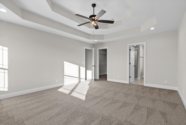 unfurnished bedroom featuring carpet floors, baseboards, a tray ceiling, and a walk in closet