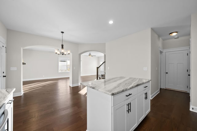 kitchen with light stone counters, arched walkways, dark wood finished floors, open floor plan, and white cabinetry