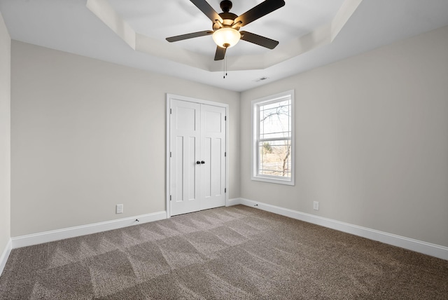 unfurnished bedroom with a tray ceiling, a closet, carpet flooring, and baseboards