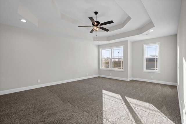 empty room with dark colored carpet, a tray ceiling, recessed lighting, and baseboards