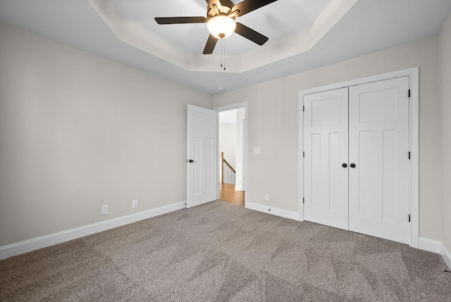 unfurnished bedroom featuring carpet floors, a tray ceiling, a closet, and baseboards