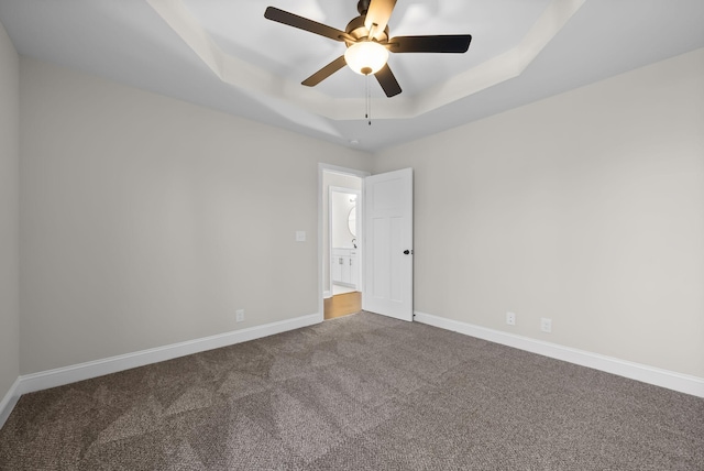 carpeted spare room with baseboards, a tray ceiling, and ceiling fan