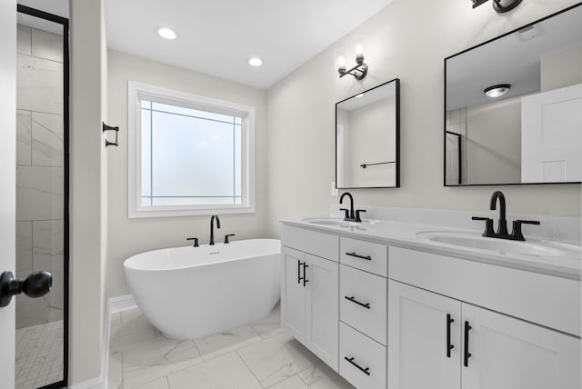 full bath featuring marble finish floor, a freestanding tub, a sink, and recessed lighting