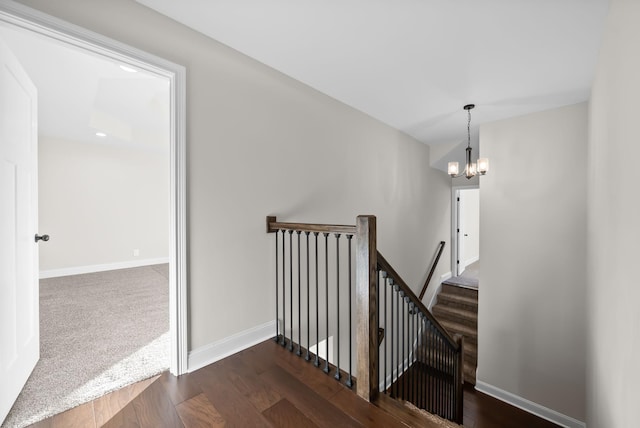 staircase with an inviting chandelier, wood finished floors, and baseboards