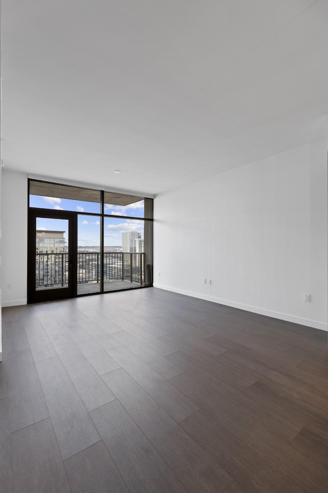 empty room with a wall of windows, dark wood-style floors, and baseboards