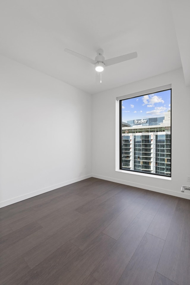 empty room with dark wood-style floors, baseboards, and ceiling fan