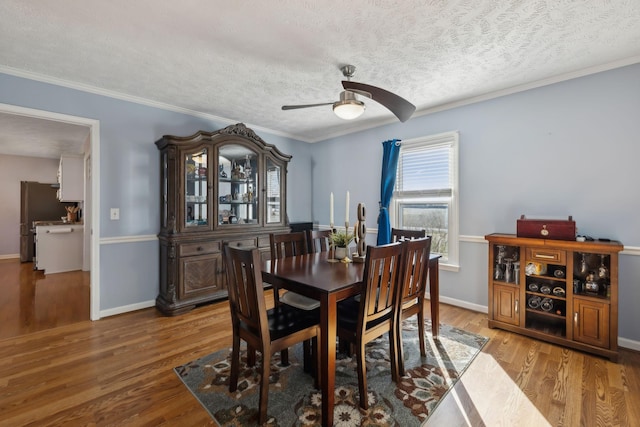 dining area featuring baseboards, ceiling fan, ornamental molding, wood finished floors, and a textured ceiling