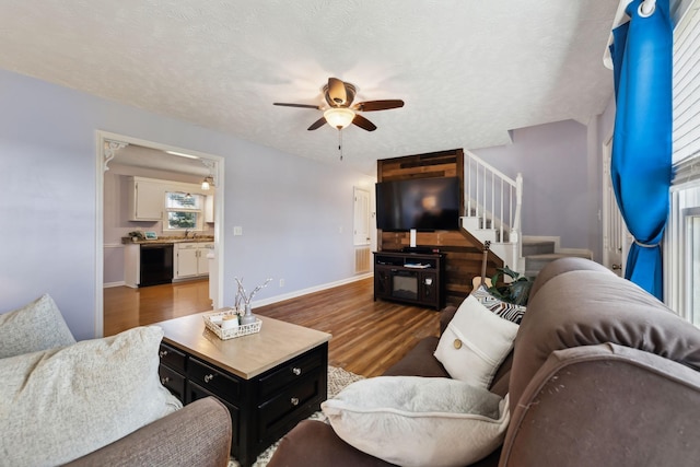 living area with baseboards, ceiling fan, wood finished floors, stairs, and a textured ceiling