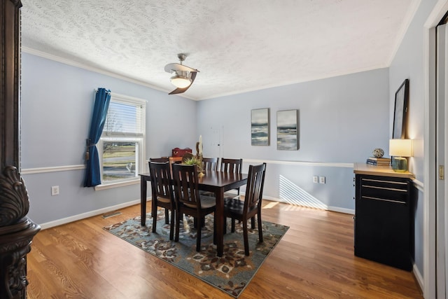 dining room with a textured ceiling, wood finished floors, visible vents, baseboards, and crown molding