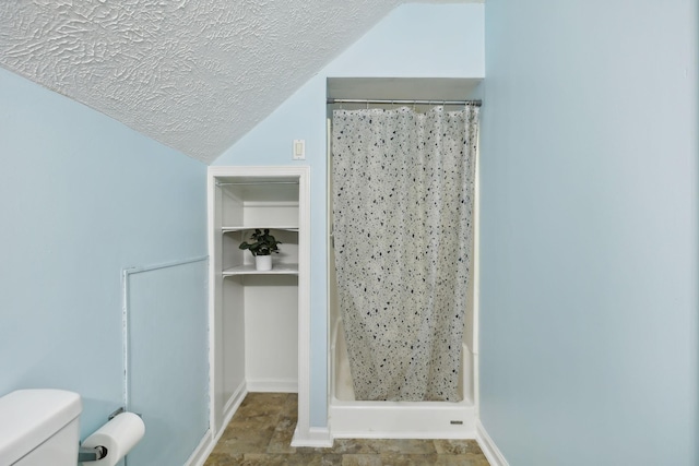 full bath with a textured ceiling, a stall shower, vaulted ceiling, and toilet