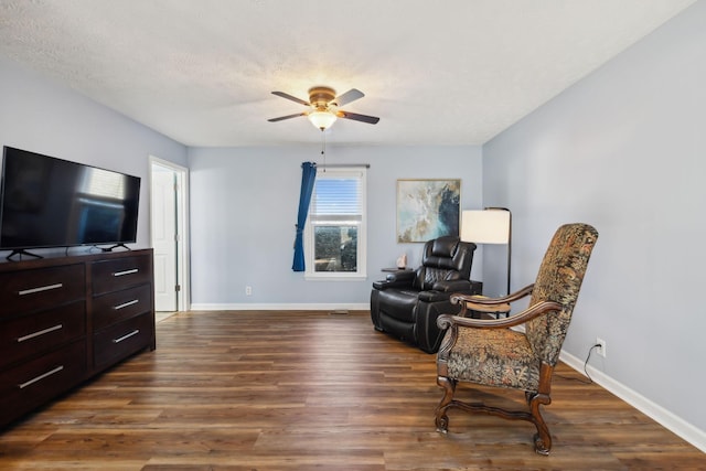 living area featuring a ceiling fan, a textured ceiling, baseboards, and dark wood-style flooring